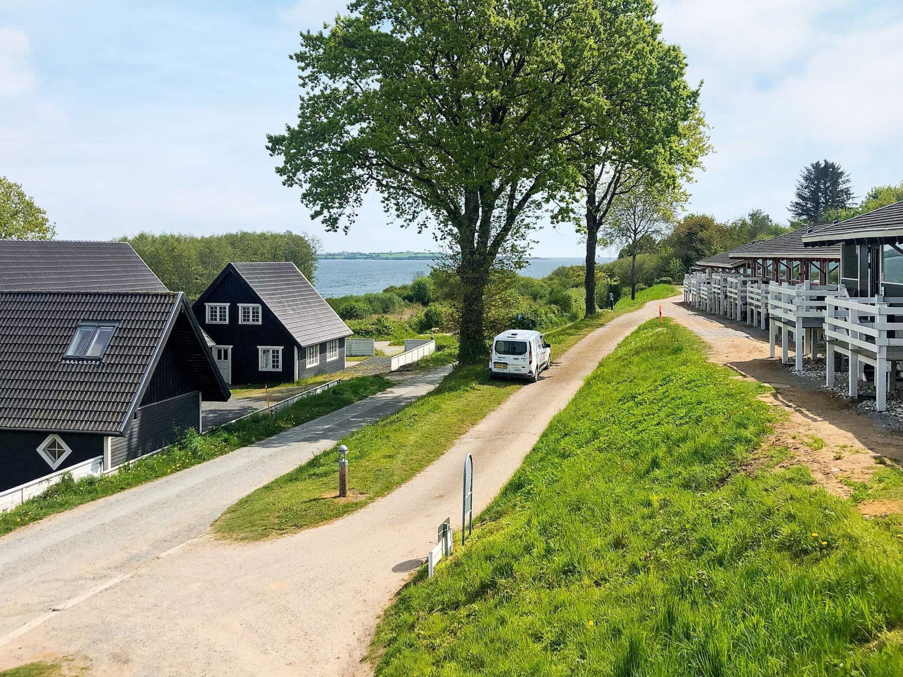 A rural setting with a dirt path, a white van, and a row of wooden cabins.