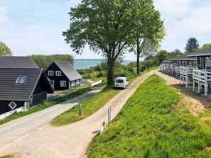 A rural setting with a dirt path, a white van, and a row of wooden cabins.