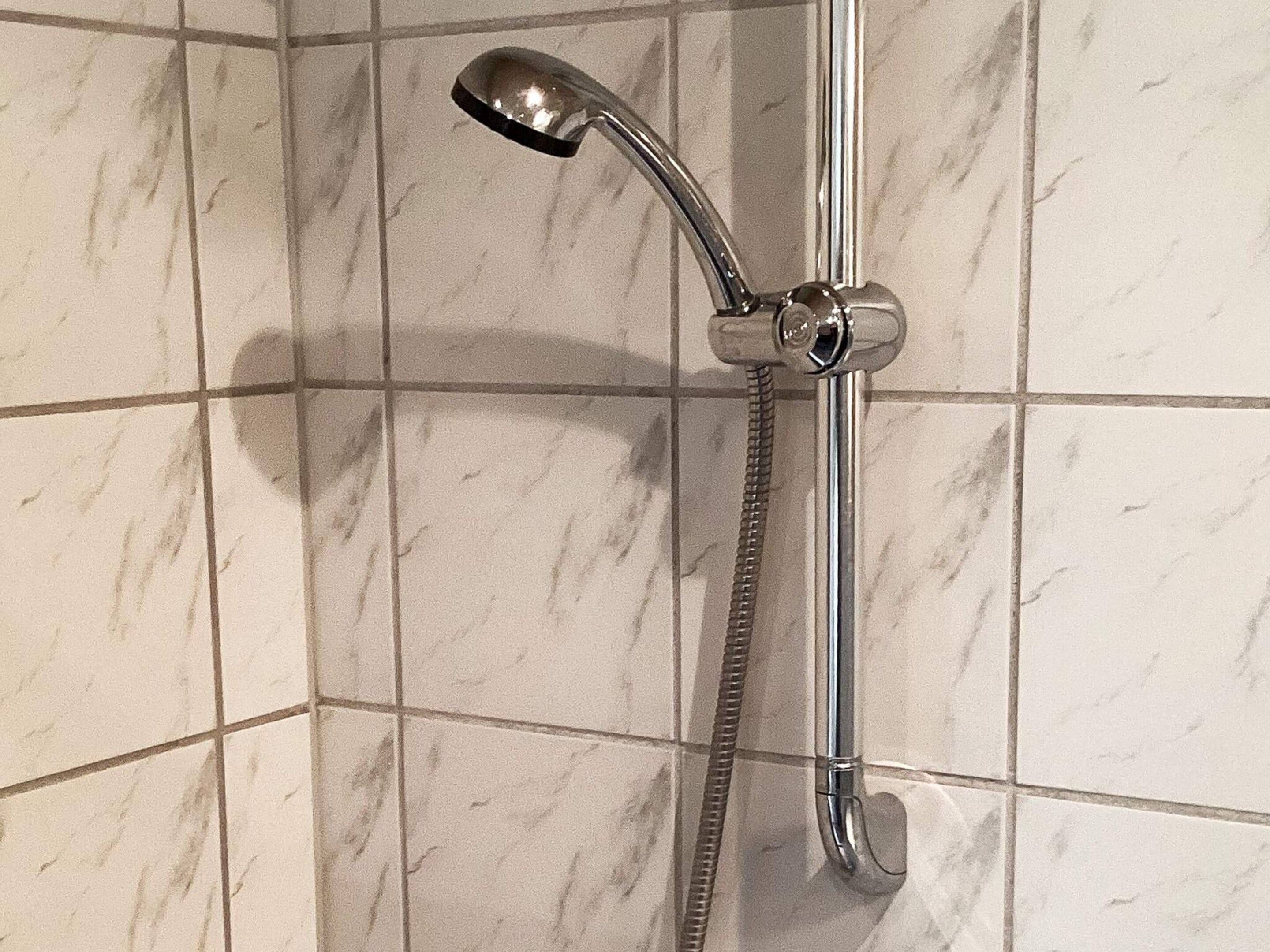 A shower with a handheld showerhead and a fixed showerhead, mounted on a wall with a tiled surface.