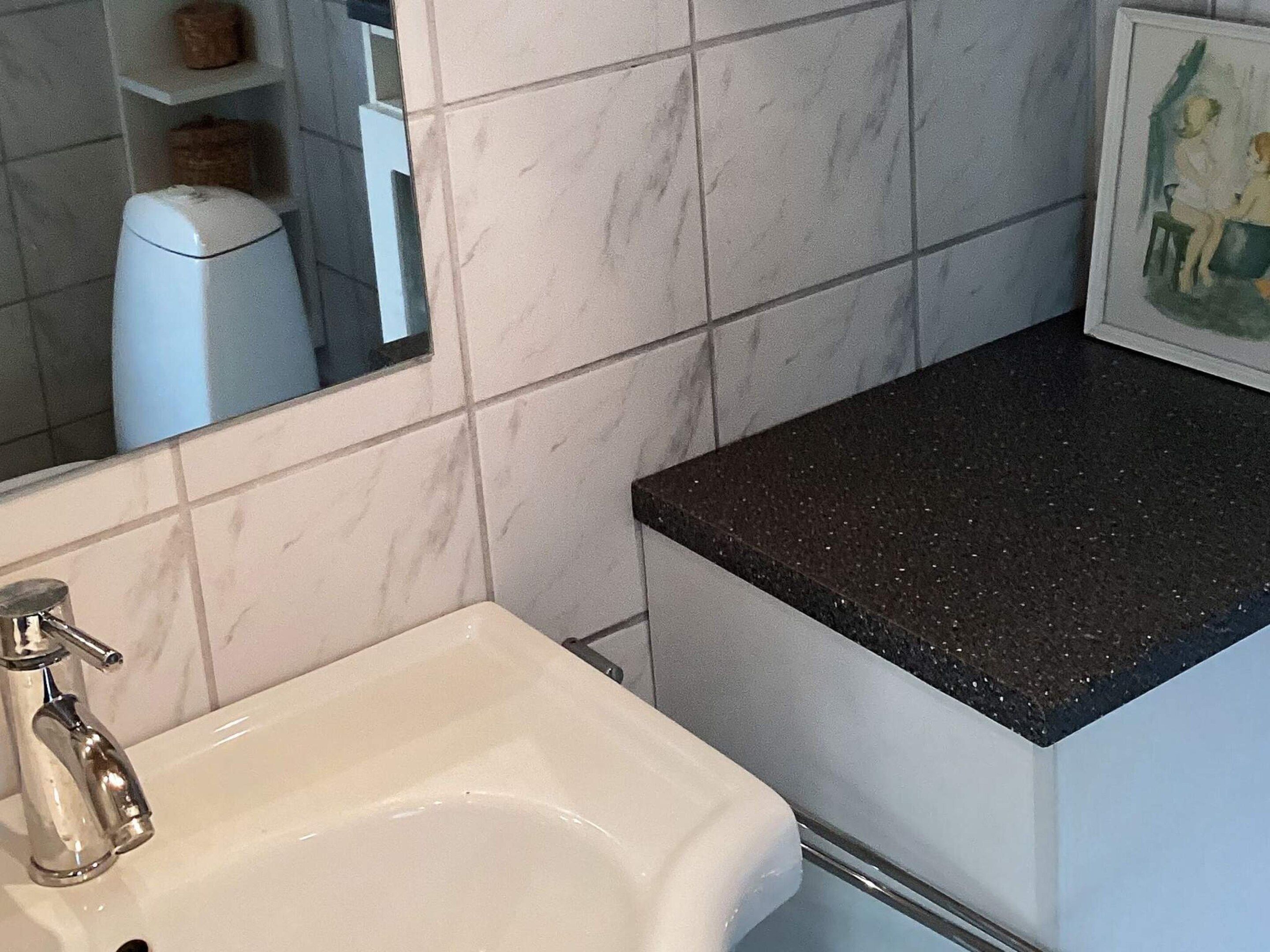 A bathroom with a white sink, a mirror, and a black countertop.