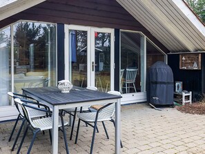 A covered patio with a table and chairs, a barbecue grill, and a sliding glass door. - 4 Person Holiday Home in Vaeggerlose (Vaeggerlose)