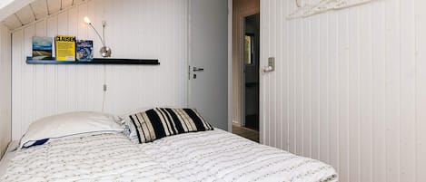 A bedroom with a bed, a door, a shelf with books, and a window.