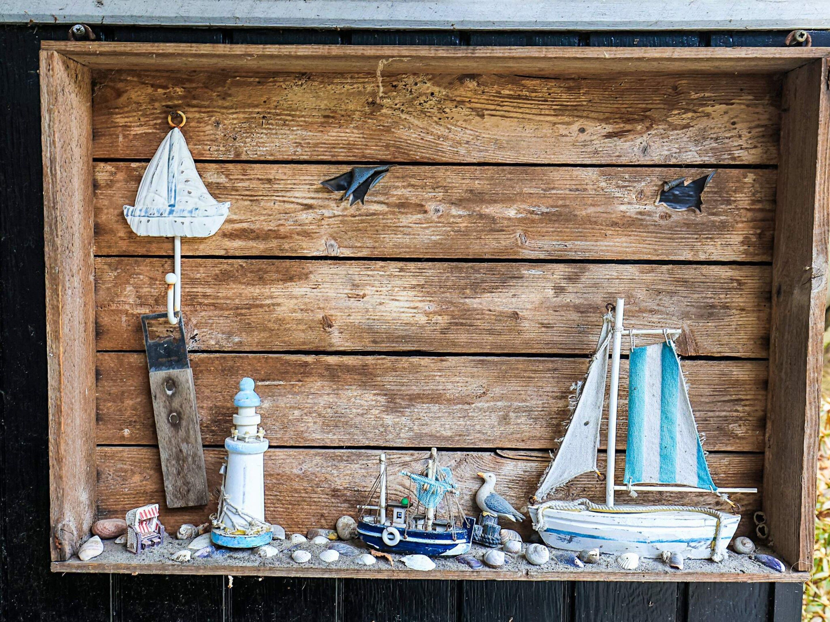 Eine Holzdarstellung mit einem Leuchtturm, einem Segelboot und Vögeln.