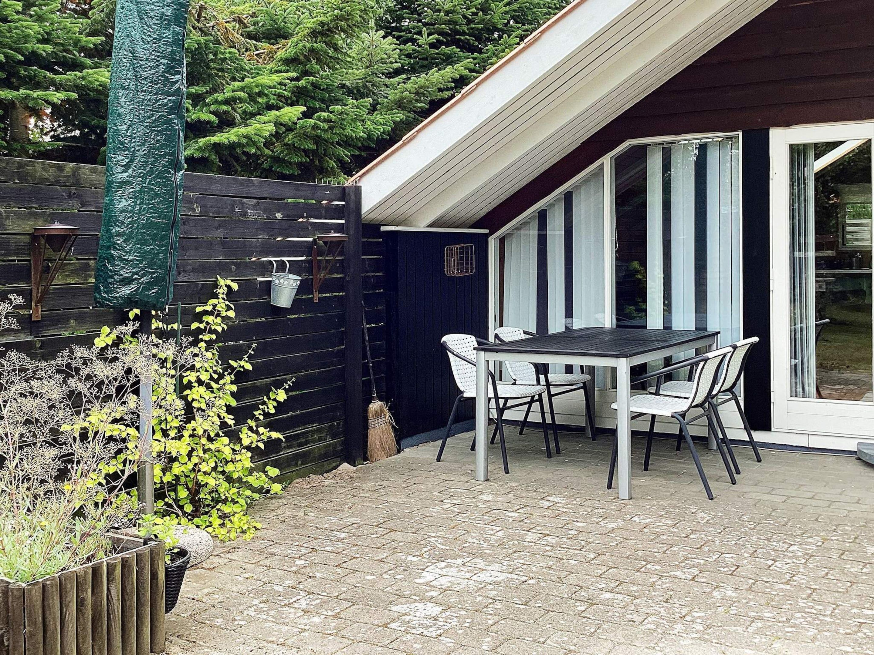A patio with a table and chairs, a wooden fence, and a green plant.