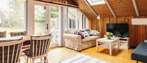 Interior acogedor de una cabaña con techo de madera, un sofá, un televisor y un comedor.