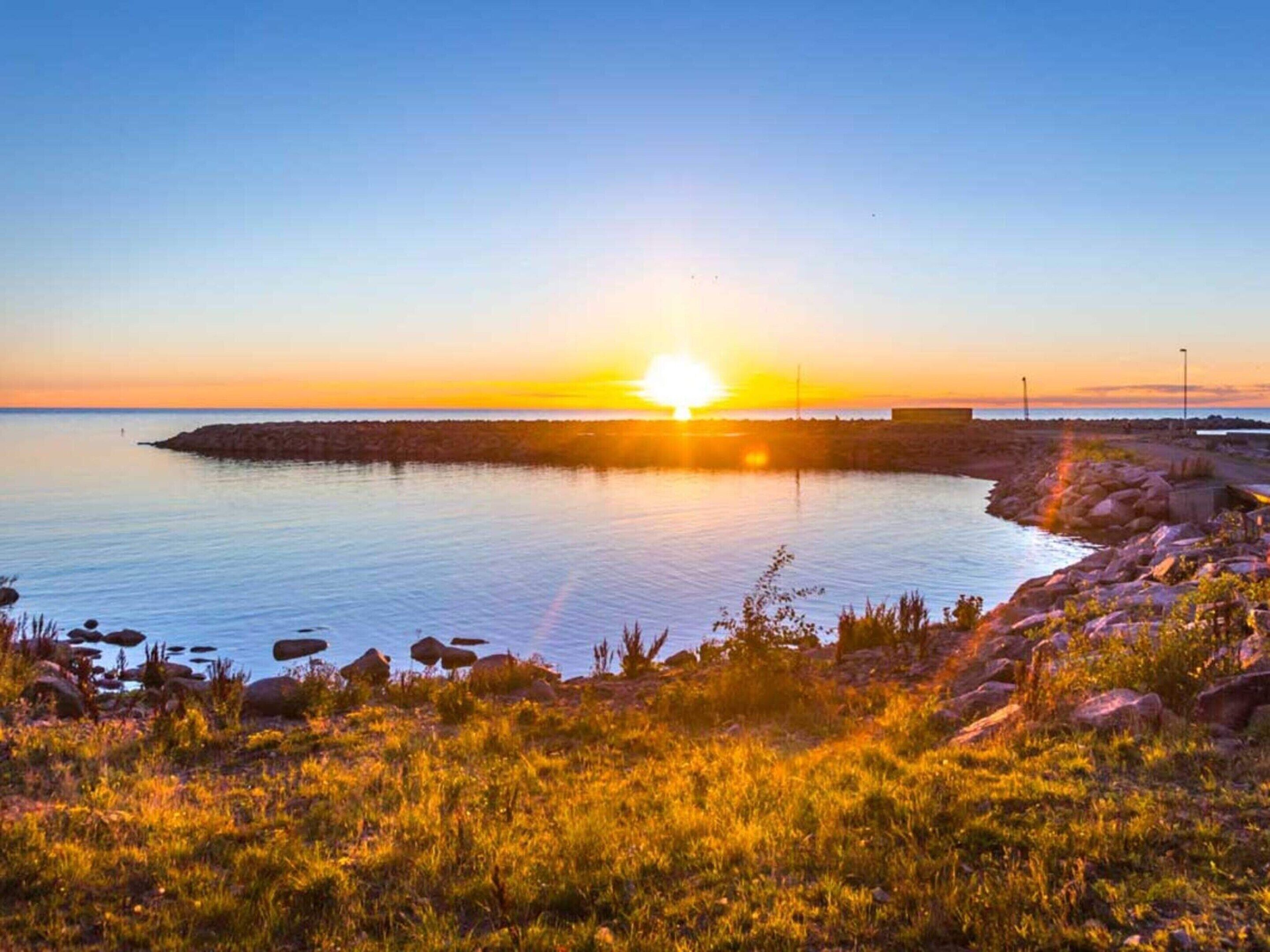 Un magnifique coucher de soleil sur la côte, avec un rivage rocheux et une eau calme.