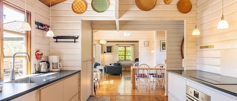 Una cocina con armarios de madera, un lavamanos y una estufa. Hay una zona de comedor con sillas y una mesa.