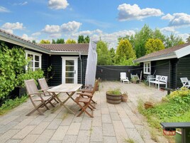 A patio area with a wooden table and chairs, a white umbrella, and a barbecue grill.