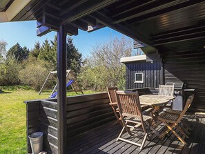 Une terrasse extérieure en bois, avec une table et des chaises, un barbecue et une aire de jeux.