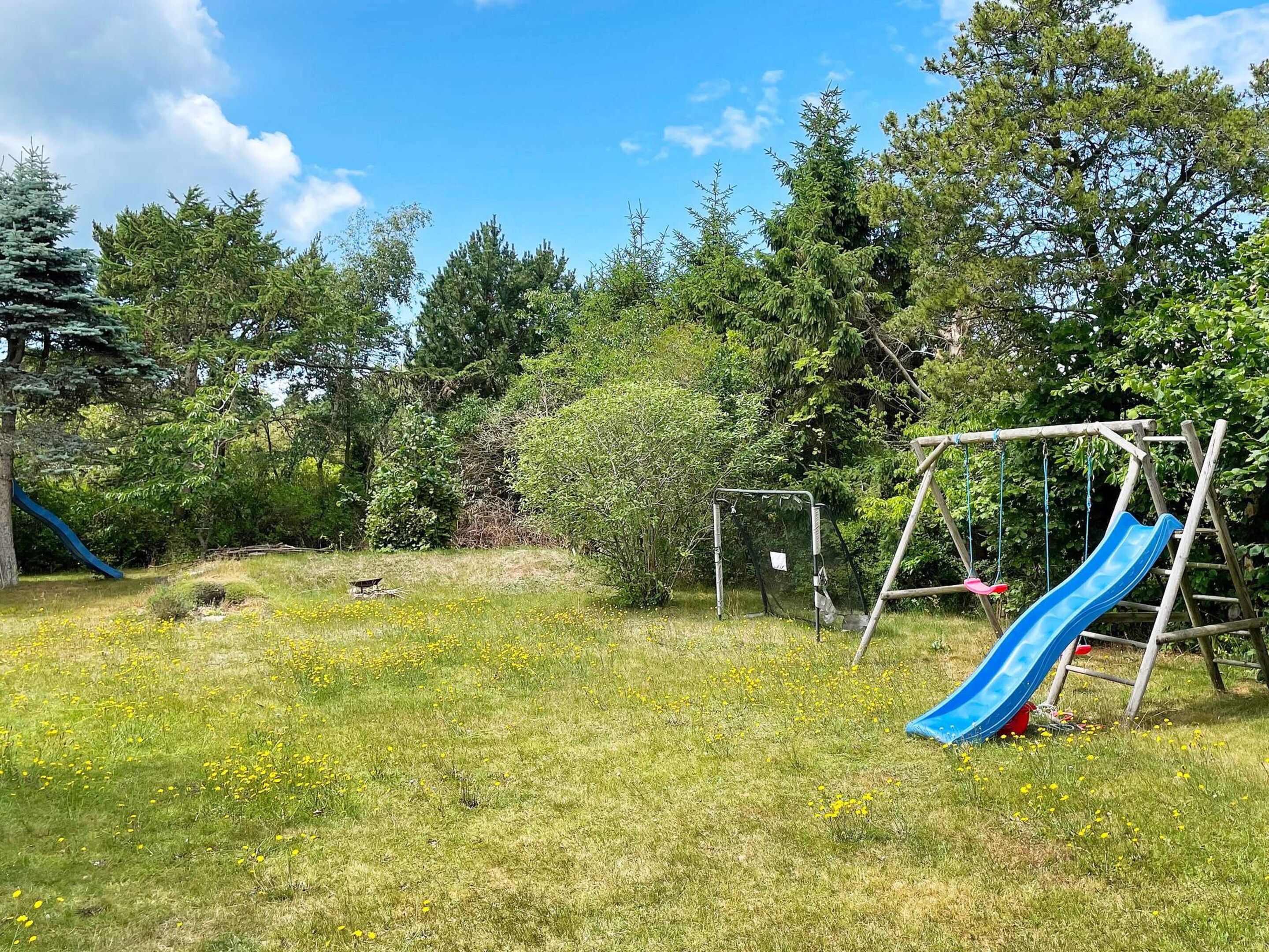 A playground with a blue slide and a swing set in a grassy area with trees.