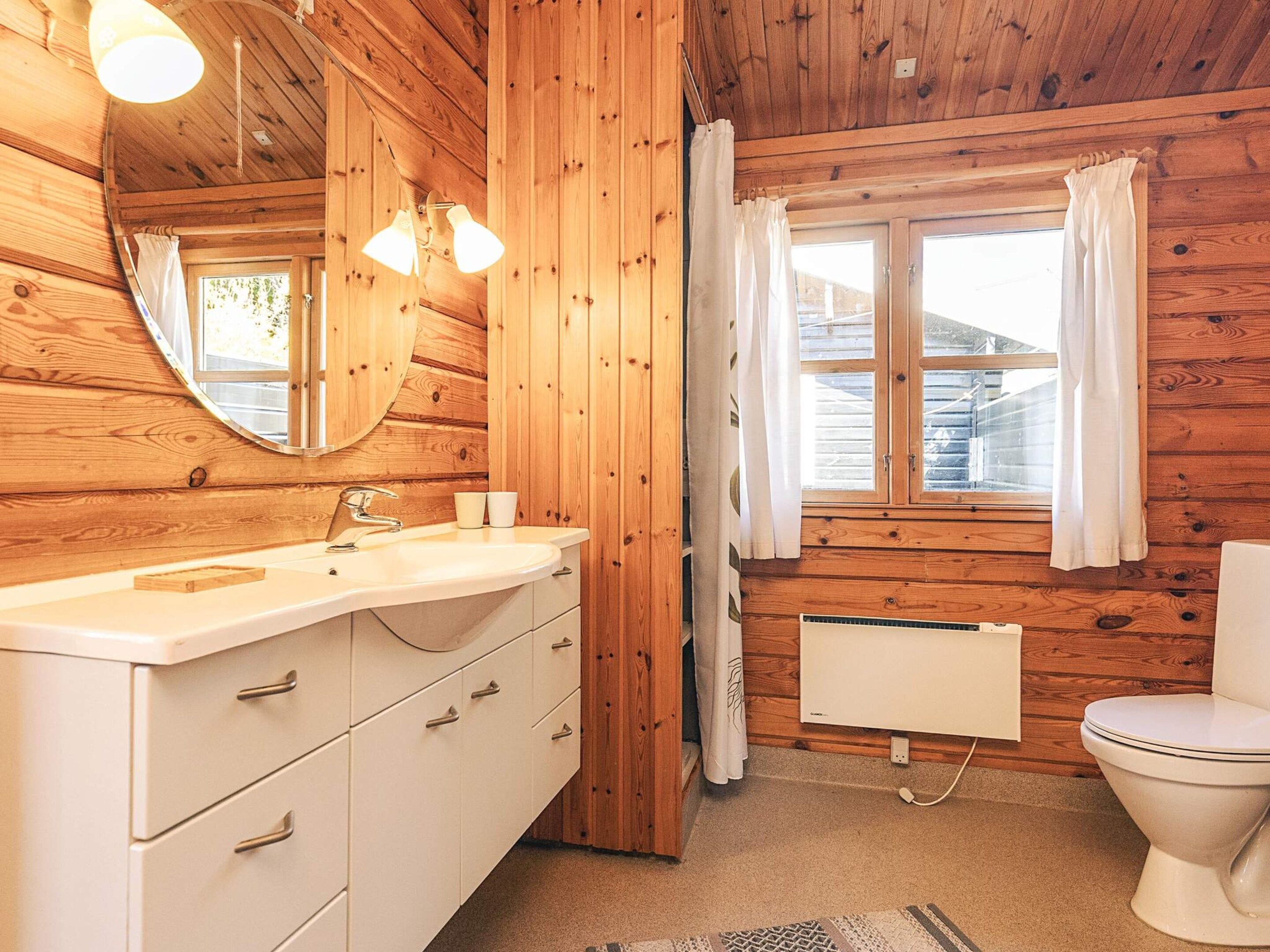 Ein Badezimmer mit Holzwandverkleidung, Waschbecken, Spiegel und Toilette.