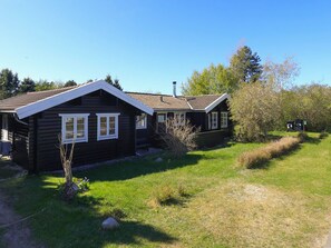 A wooden cabin with a sloped roof, surrounded by a grassy area and trees.