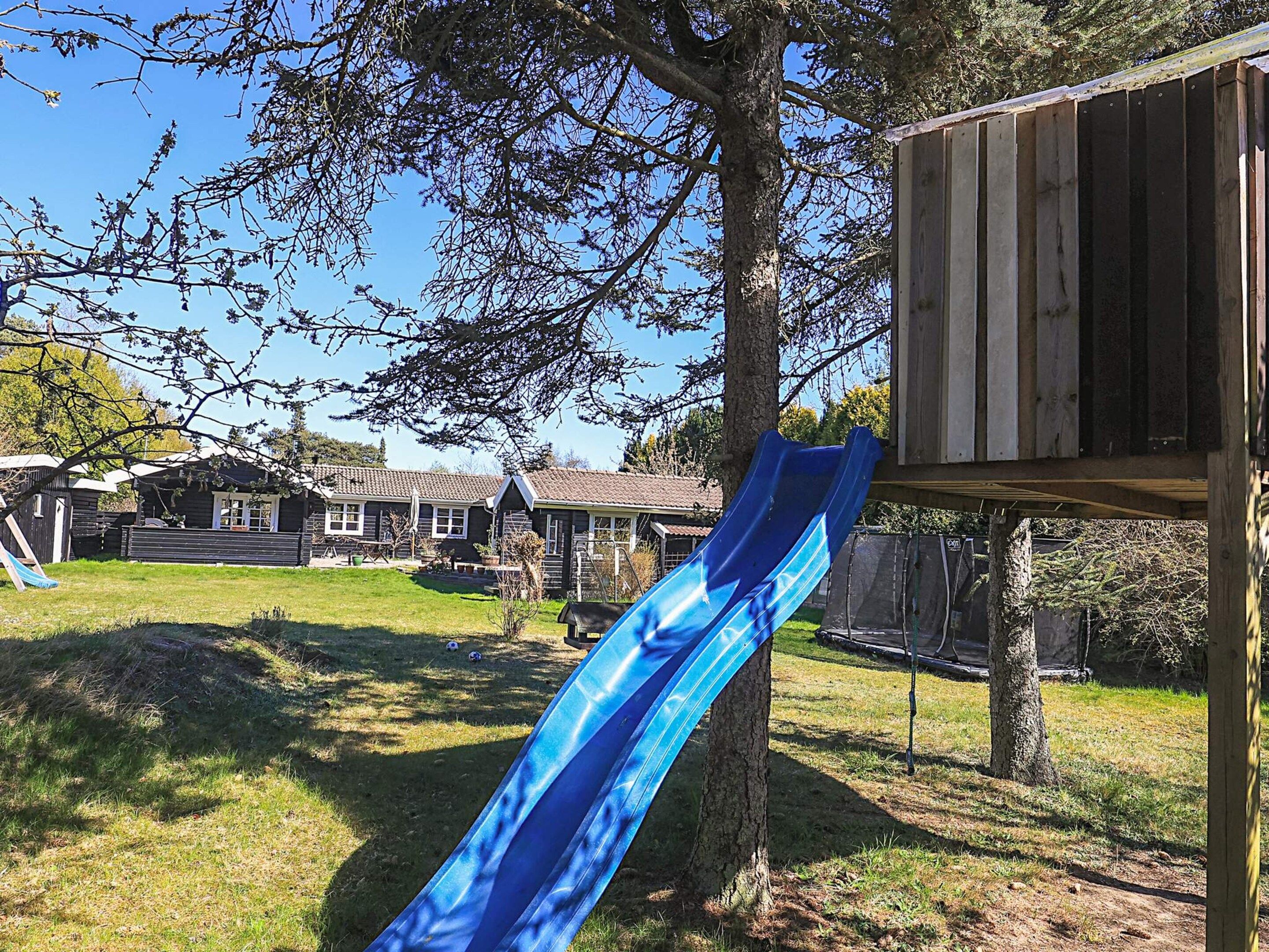 A backyard with a blue slide, a wooden playhouse, and a grassy area with trees.