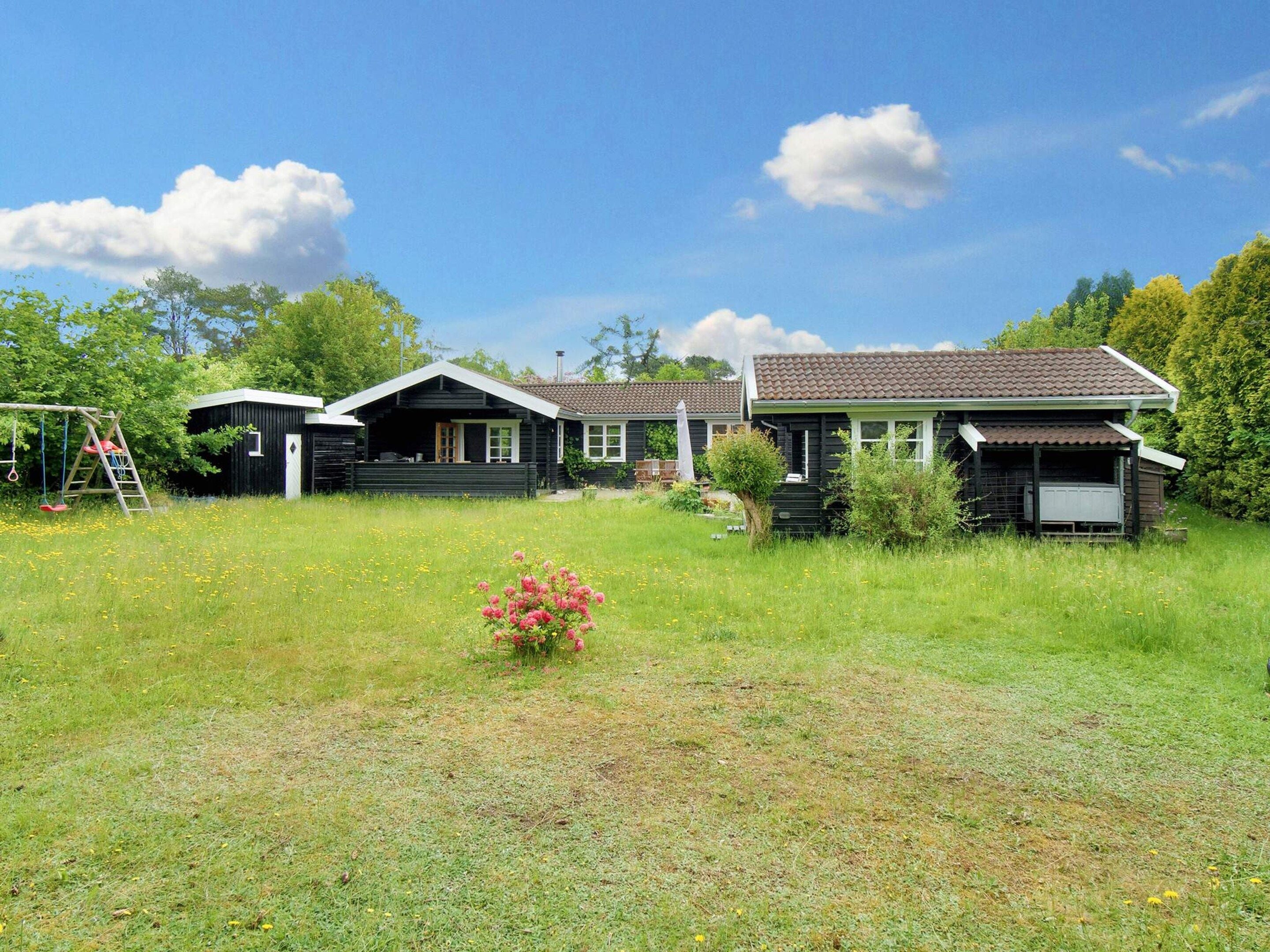 A two-story wooden house with a porch, surrounded by a grassy yard and trees.