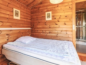 A wooden cabin room with a bed, framed pictures on the walls, and a shower area.