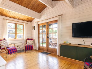 A room with wooden floors, a television, wicker chairs, a bench, and a large window.