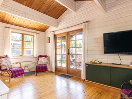 Una habitación con piso de madera, televisor, sillas de mimbre, un banco y un ventanal grande.