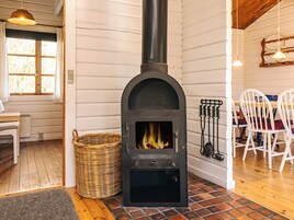 Una habitación acogedora con estufa de leña, cesta de mimbre y sillas blancas.