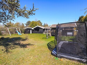 A residential area with a trampoline, a swing set, and a small house with a tiled roof.