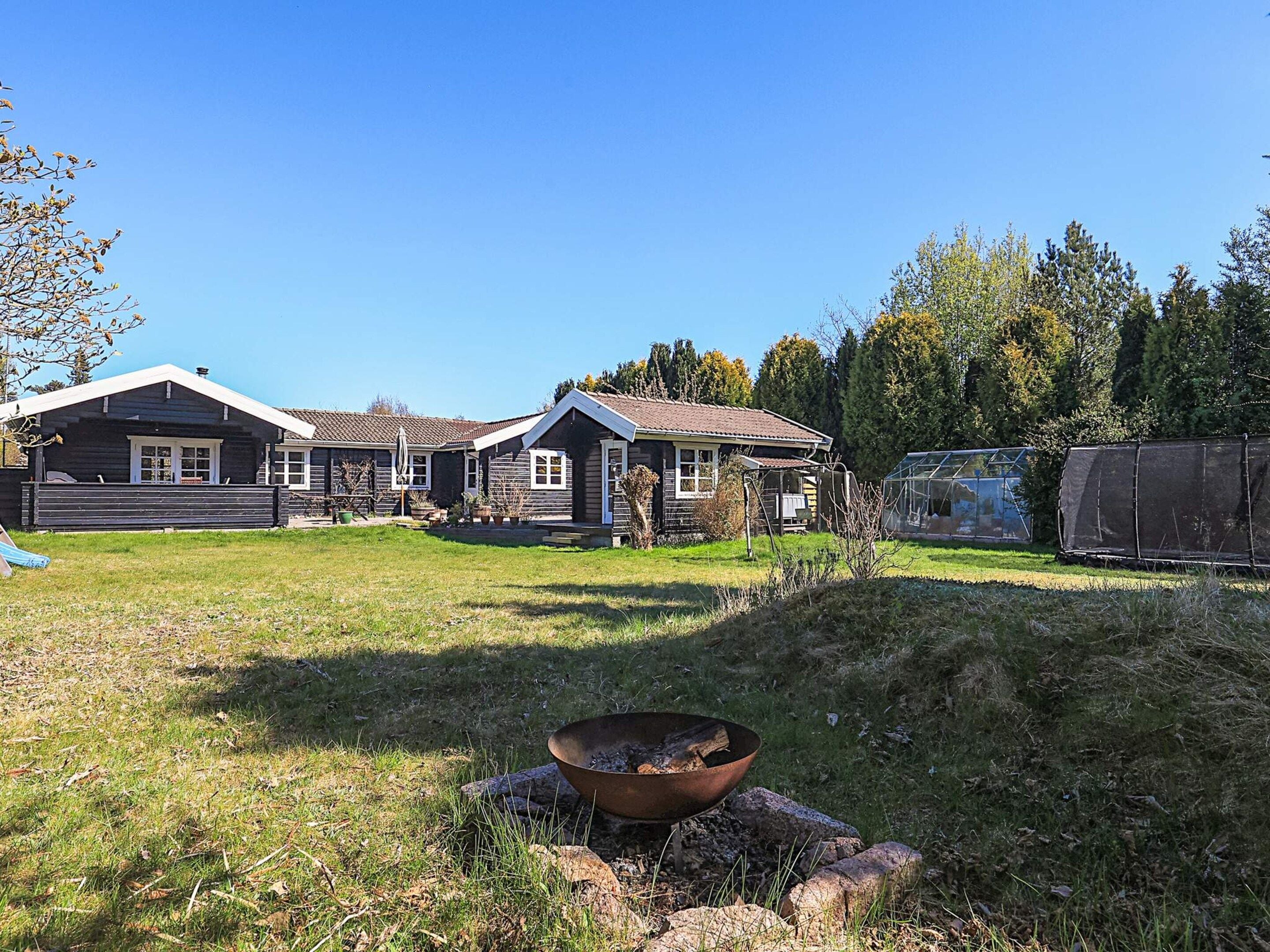 A two-story wooden house with a covered porch and a fire pit in the yard.