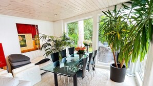 A modern living room with a glass dining table, black chairs, a white sofa, and a large potted plant. - 10 Person Holiday Home in Arendal-by Traum (Arendal)