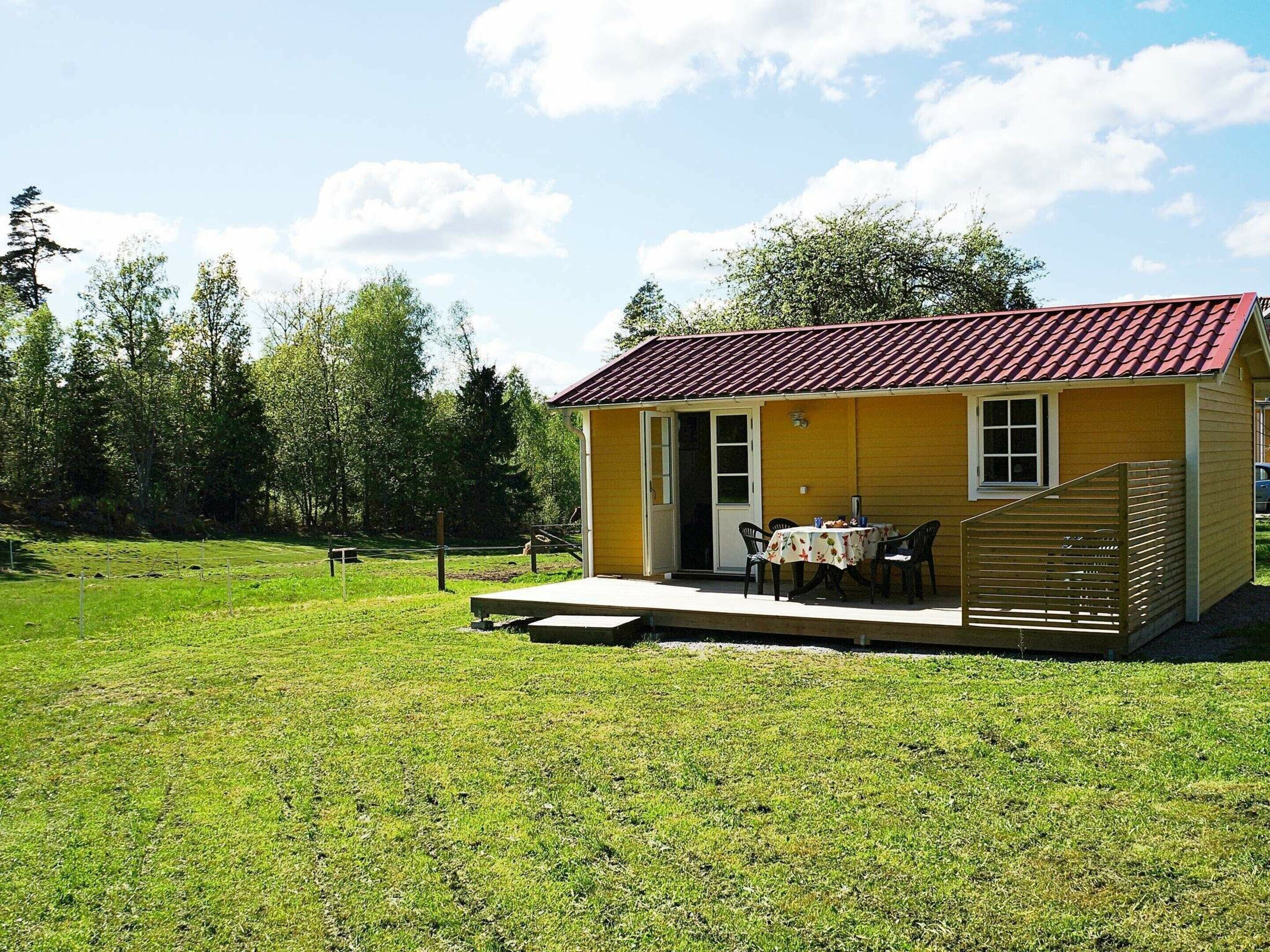 A small yellow building with a red roof, a covered patio with a table and chairs, and a grassy yard.