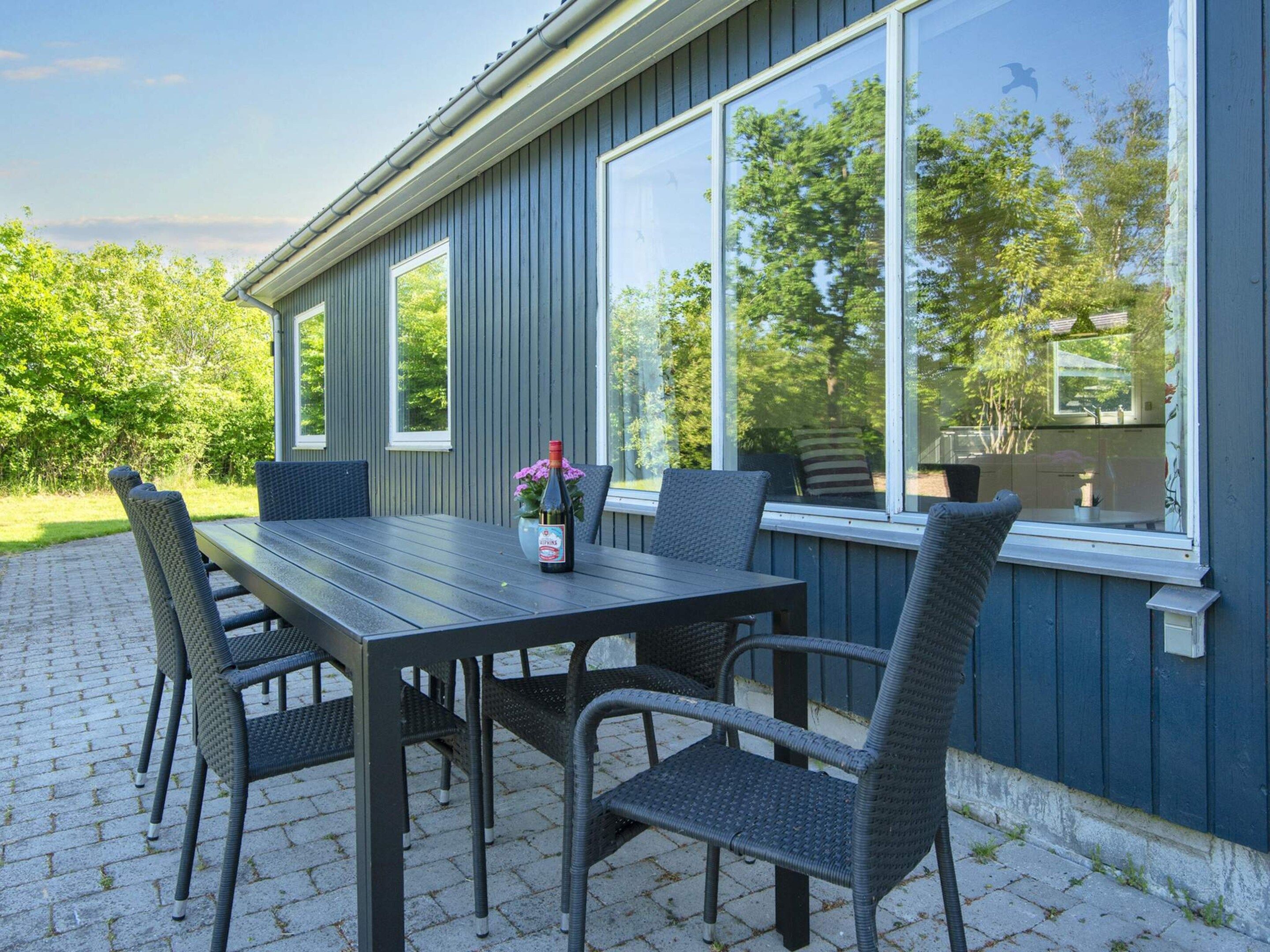 Un patio al aire libre con una mesa, sillas, una botella de bebida y una ventana con vista a la vegetación.