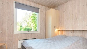 A bedroom with a bed, a window, a radiator, and a wooden wall.