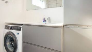 Un lavadero pequeño con lavadora de carga frontal, un lavabo y un espejo encima.