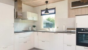 A modern kitchen with white cabinets, a black countertop, a built-in oven, and a window with blinds.