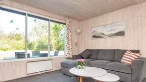 A room with a grey sofa, a white coffee table, and a window with a view of greenery.