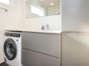 Een kleine wasruimte met een voorlader wasmachine, een wasbak en een spiegel erboven.