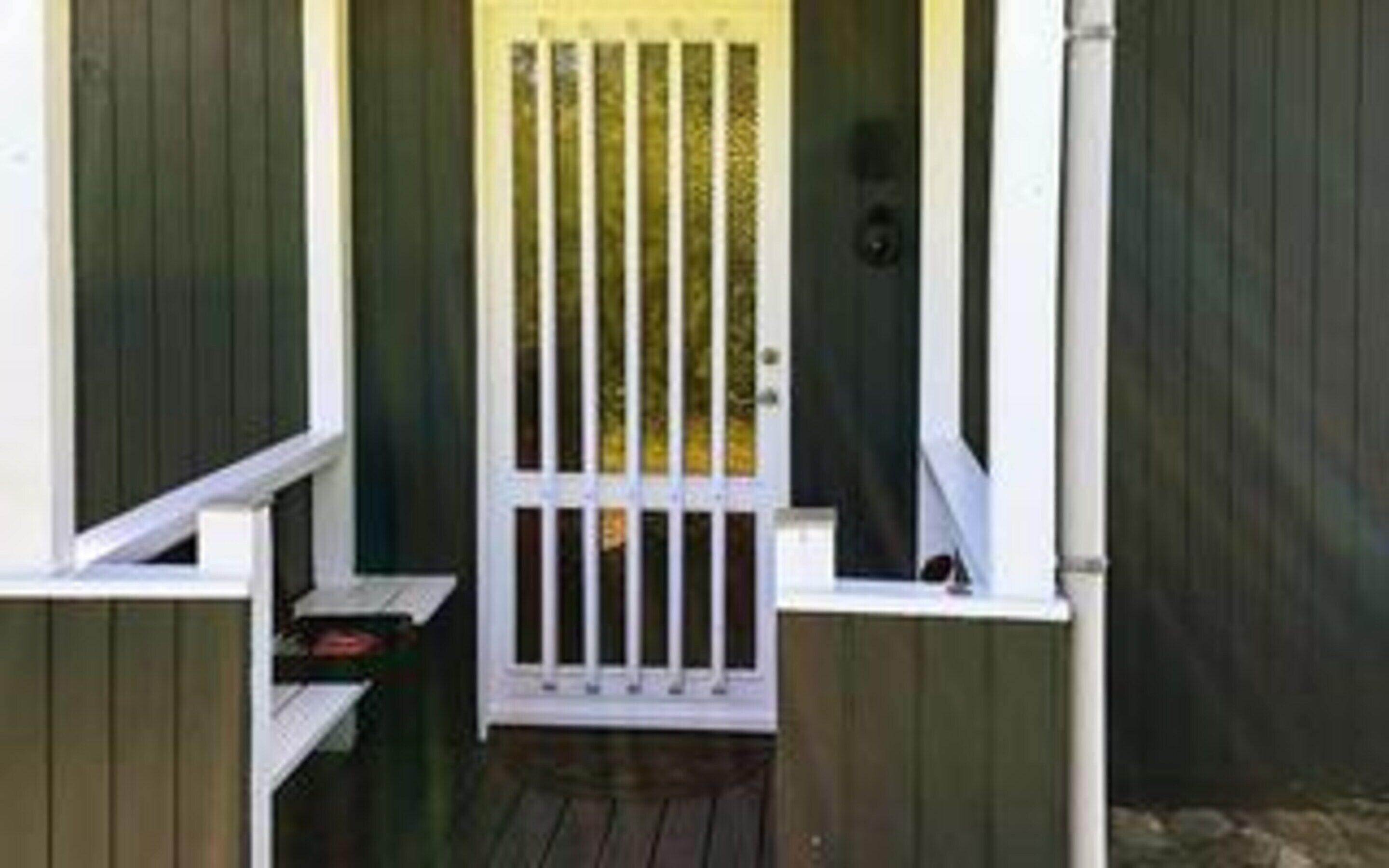 A wooden door with vertical bars, a small porch with a bench, and a dark wooden wall.
