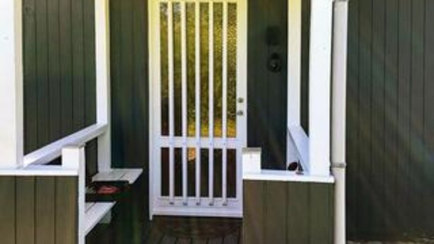 A wooden door with vertical bars, a small porch with a bench, and a dark wooden wall.