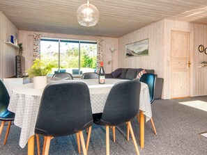 A dining area with a table set for four, surrounded by black chairs with wooden legs. There is a bottle of wine on the table, and a plant is visible on the left side. - 5 Person Holiday Home in Bording (Bording)