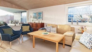 A modern living room with a wooden ceiling, a sofa, a coffee table, and a view of a brick building through a window. - 8 Person Holiday Home in Skagen (Skagen)