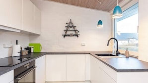 A modern kitchen with white cabinets, a black countertop, a built-in oven, a sink with a black faucet, and a blue pendant light. - 8 Person Holiday Home in Skagen (Skagen)