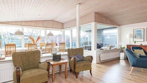 A spacious living room with wooden floors and furniture, large windows offering a view of the outdoors, and a modern design aesthetic. - 8 Person Holiday Home in Skagen (Skagen)