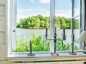 A window with a view of a lake and greenery, a candelabra with candles, and a lamp on the windowsill.