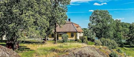 Une maison avec un toit en tuiles, entourée d’arbres et d’un terrain herbeux.