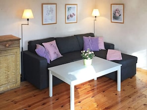 A living room with a dark-colored sofa, two purple pillows, a white coffee table, and a wooden cabinet. - 5 Person Holiday Home in Flen (Flen)