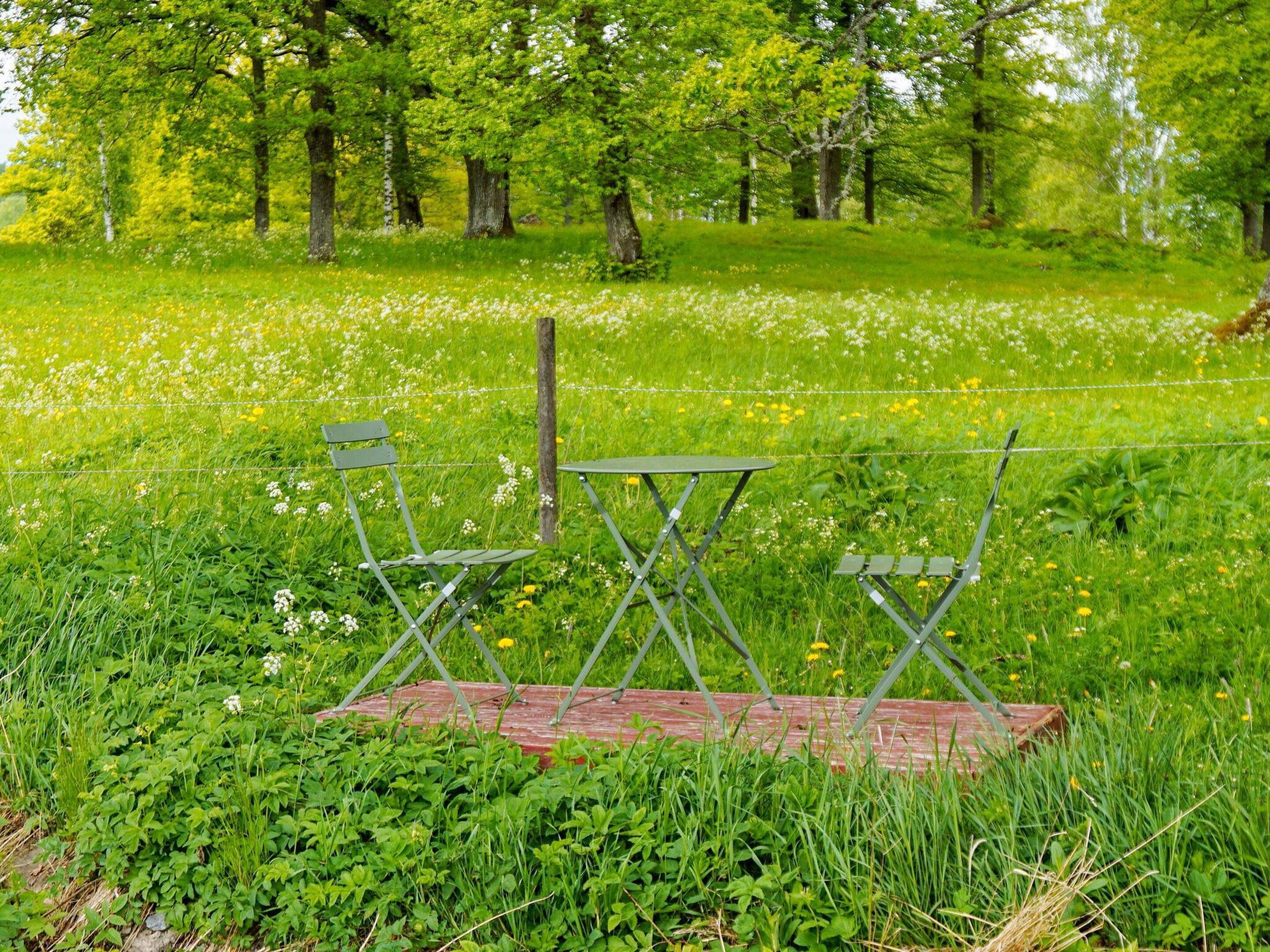 A grassy field with a wooden bench and two green folding chairs.