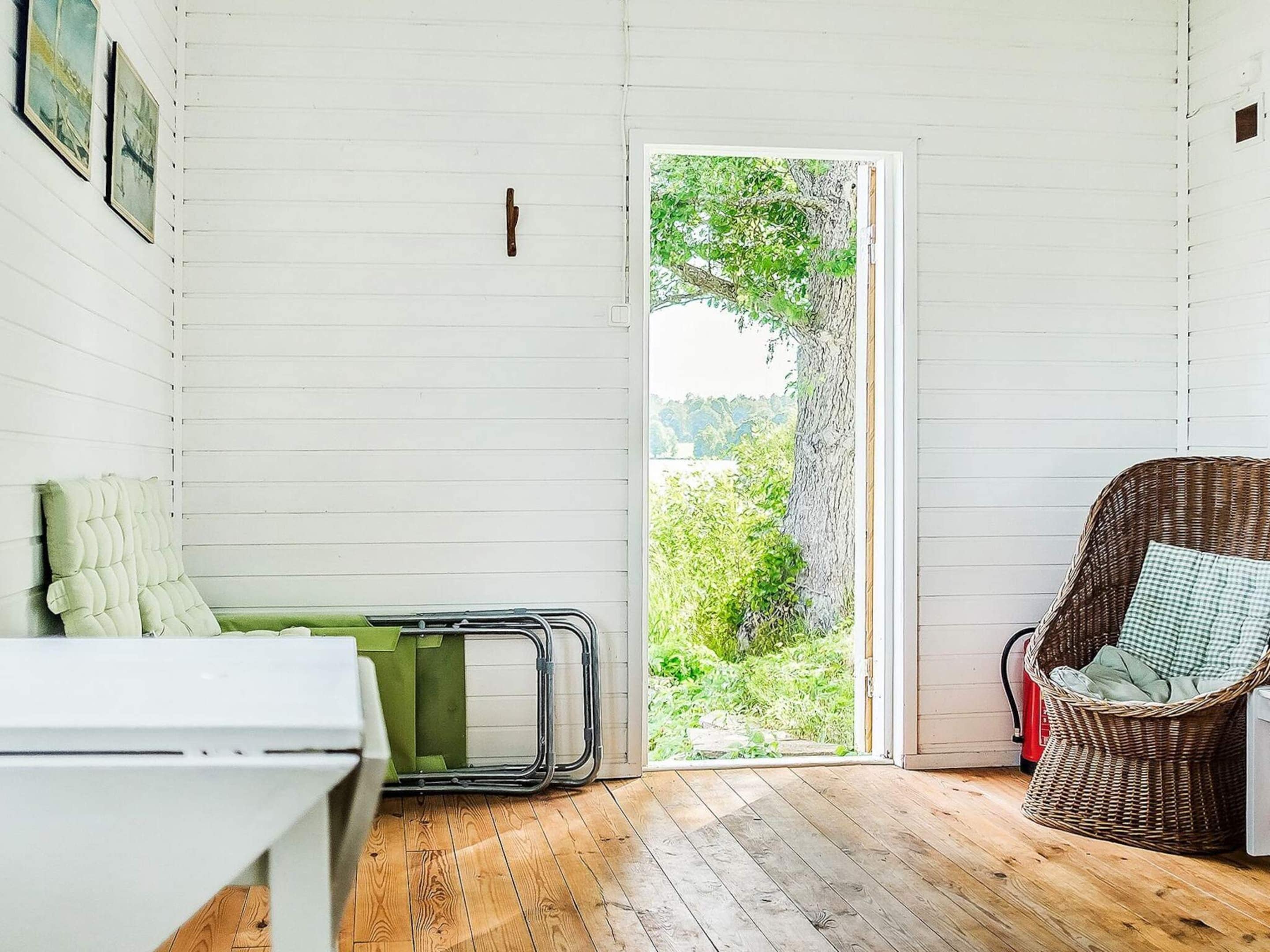 A room with a wooden floor, a wicker chair, a green bench, and a door leading outside.