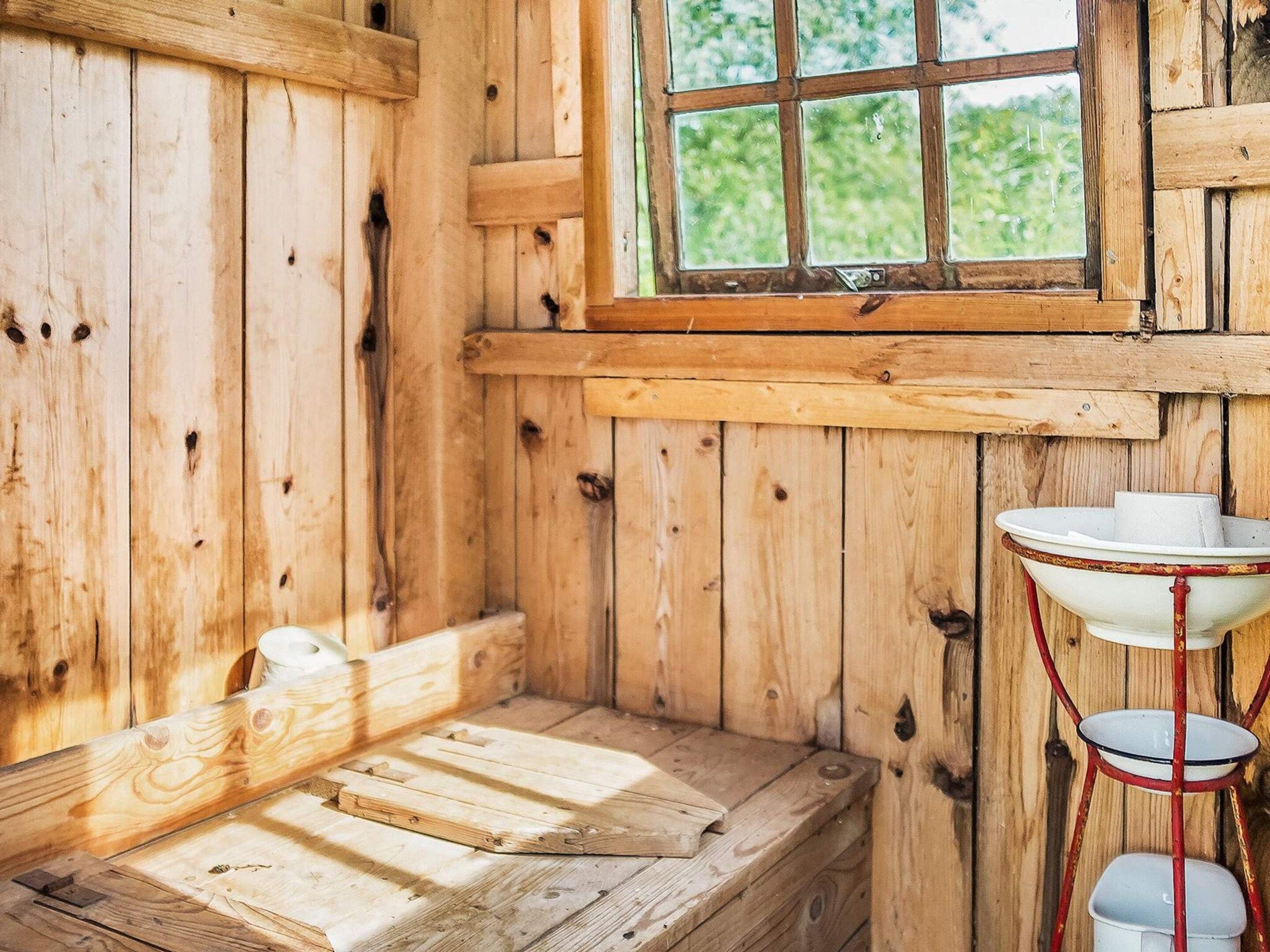 A rustic wooden cabin interior with a bench, a window, and a metal sink.