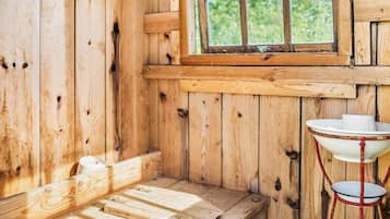 Interior rústico de una cabaña de madera con un banco, una ventana y un lavamanos de metal.