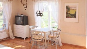 Una habitación con piso de madera, muebles blancos, un televisor en una cómoda y un cuadro en la pared.