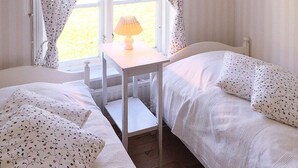 Un dormitorio con dos camas, una mesita de noche con lámpara y una ventana con cortinas.