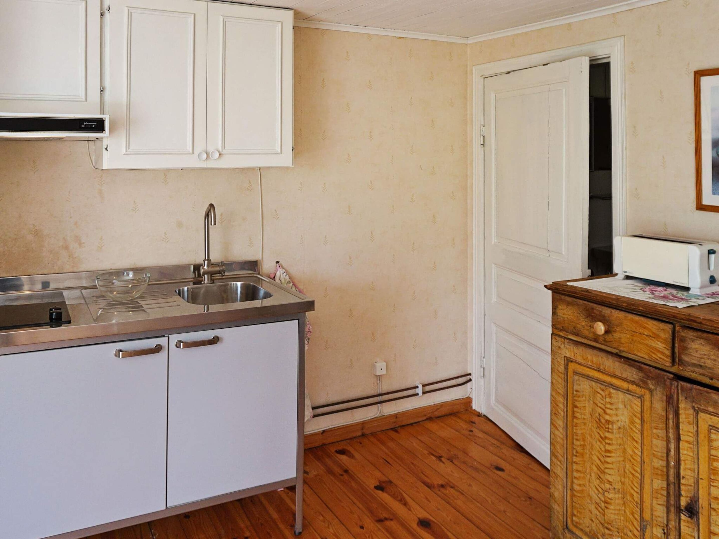 A compact kitchen with white cabinets, a stainless steel sink, and a wooden cabinet with a toaster.
