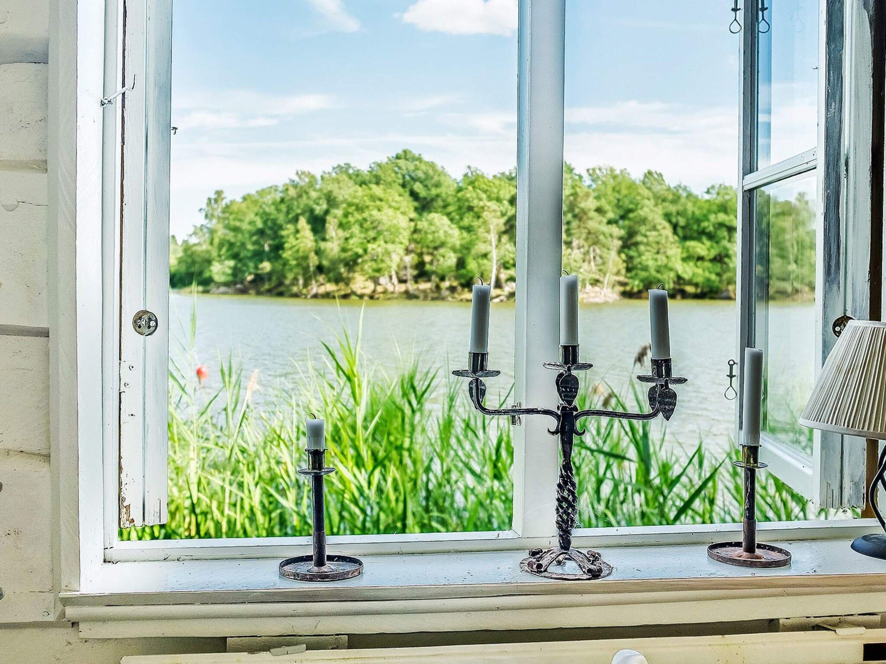 Ein Fenster mit Blick auf einen See und viel Grün, ein Kandelaber mit Kerzen und eine Lampe auf dem Fensterbrett.