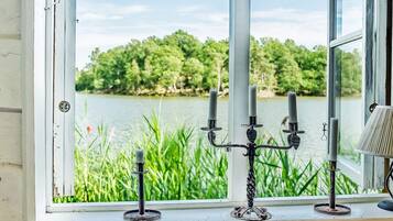Ein Fenster mit Blick auf einen See und viel Grün, ein Kandelaber mit Kerzen und eine Lampe auf dem Fensterbrett.